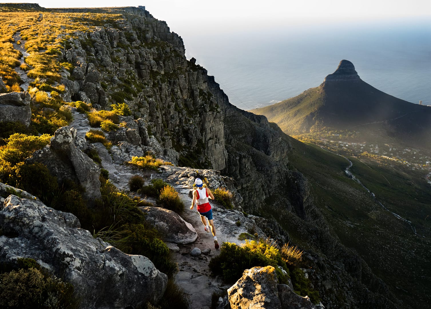 Trail runner running along a trail on the top of Table Mountain in Cape Town while out training in the mountains at sunset